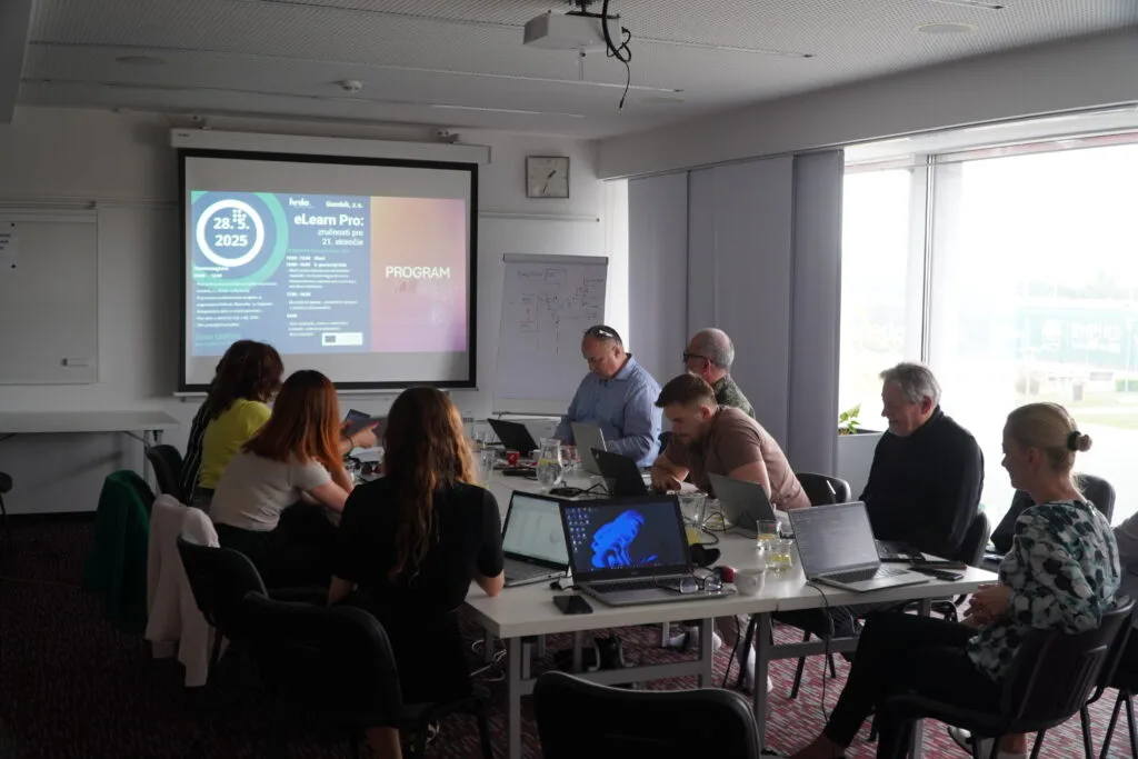 Účastníci workshopu pri stoloch s notebookmi a prezentáciou